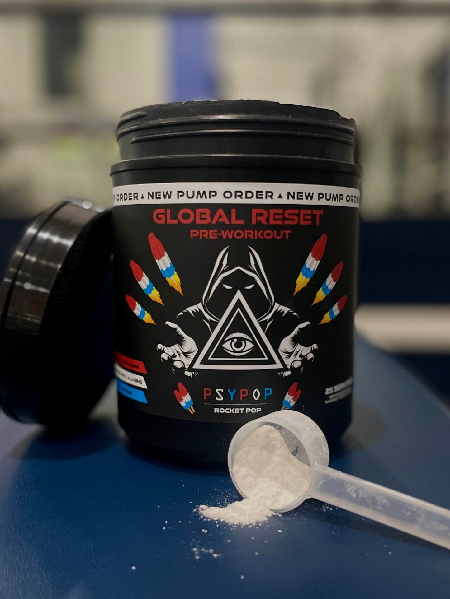 Pre-workout supplement container with scoop of powder on a blue surface